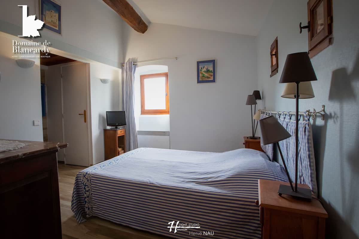 A bedroom with a bed, a desk, a lamp, and a window.