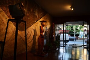 Uma área de recepção com uma estátua, uma parede com textura e uma porta de vidro que dá para o exterior.