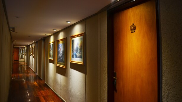 Un pasillo de hotel con obras enmarcadas en las paredes, una puerta de madera con un número y un piso de madera pulida.