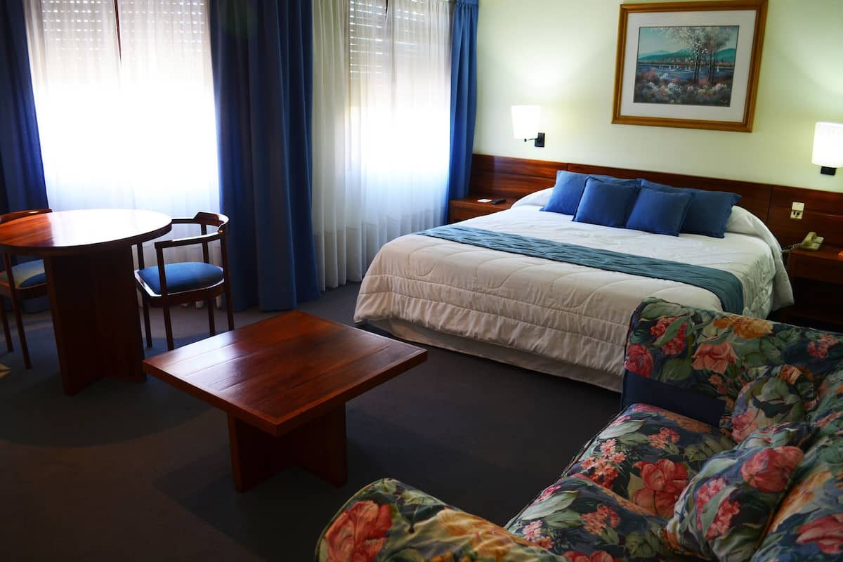 Une chambre d’hôtel avec un lit, un bureau en bois, une chaise, un canapé et un tableau au mur.