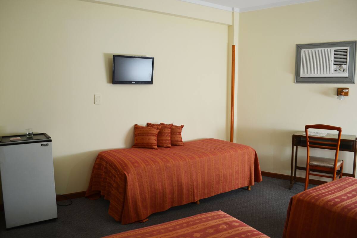 Une chambre d’hôtel équipée d’un lit, d’un bureau, d’une chaise, d’une télévision et d’un petit réfrigérateur.