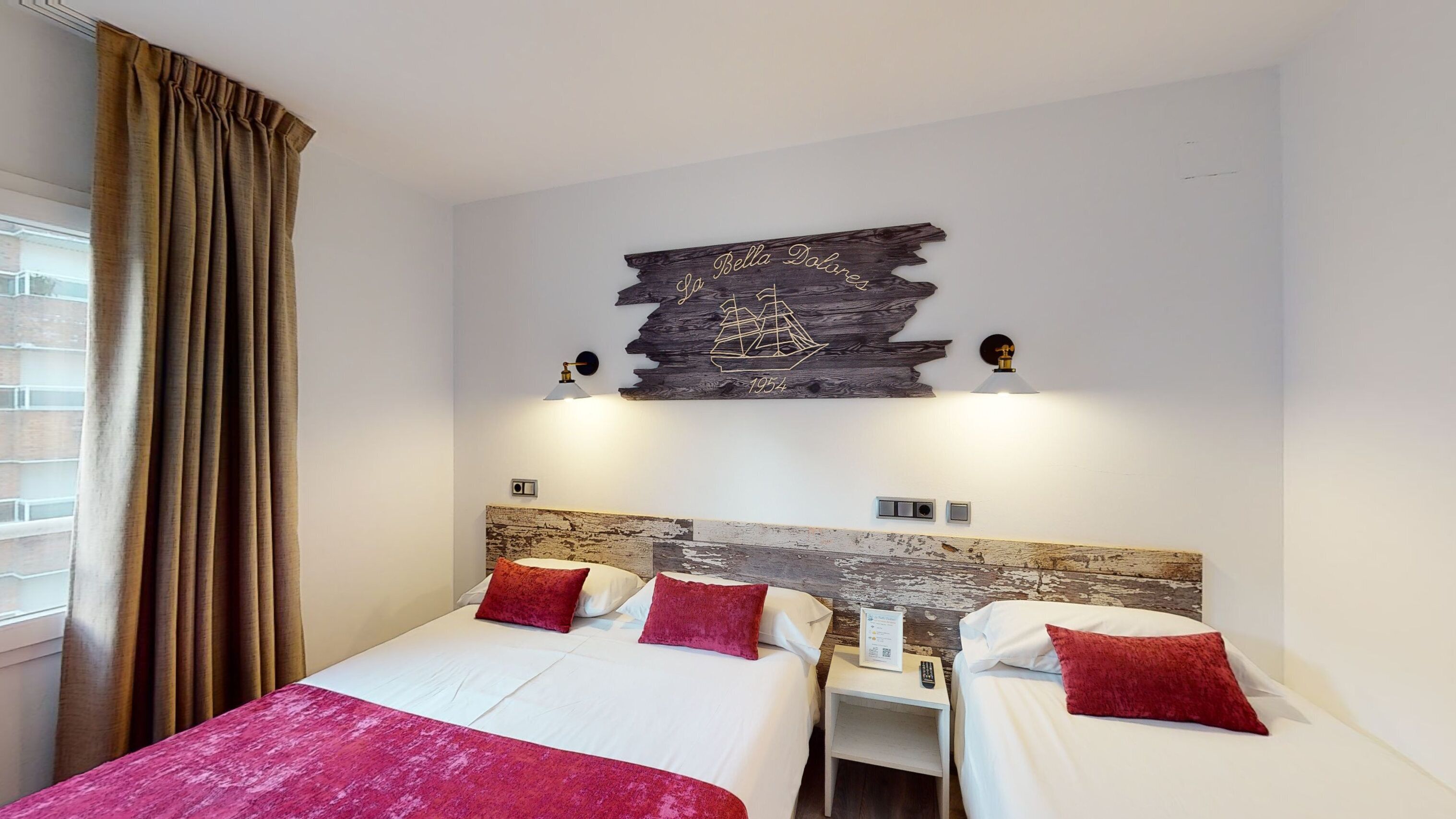 A hotel room with two beds, a wooden headboard, a wall-mounted artwork, and a window with curtains.