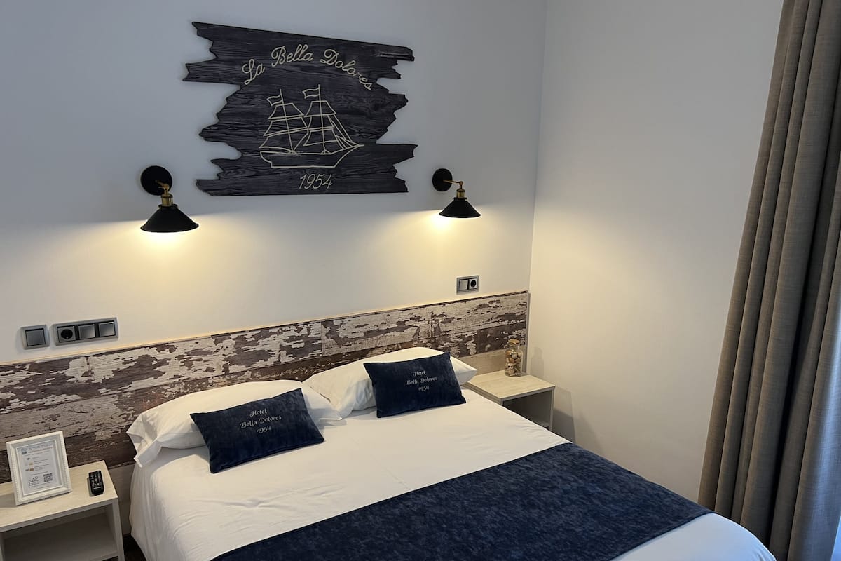 Habitación de hotel con cama, dos mesitas de noche, un adorno de barco en la pared y dos lámparas de pared.