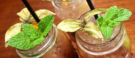 Three mason jars with mint leaves and black straws on a wooden table.