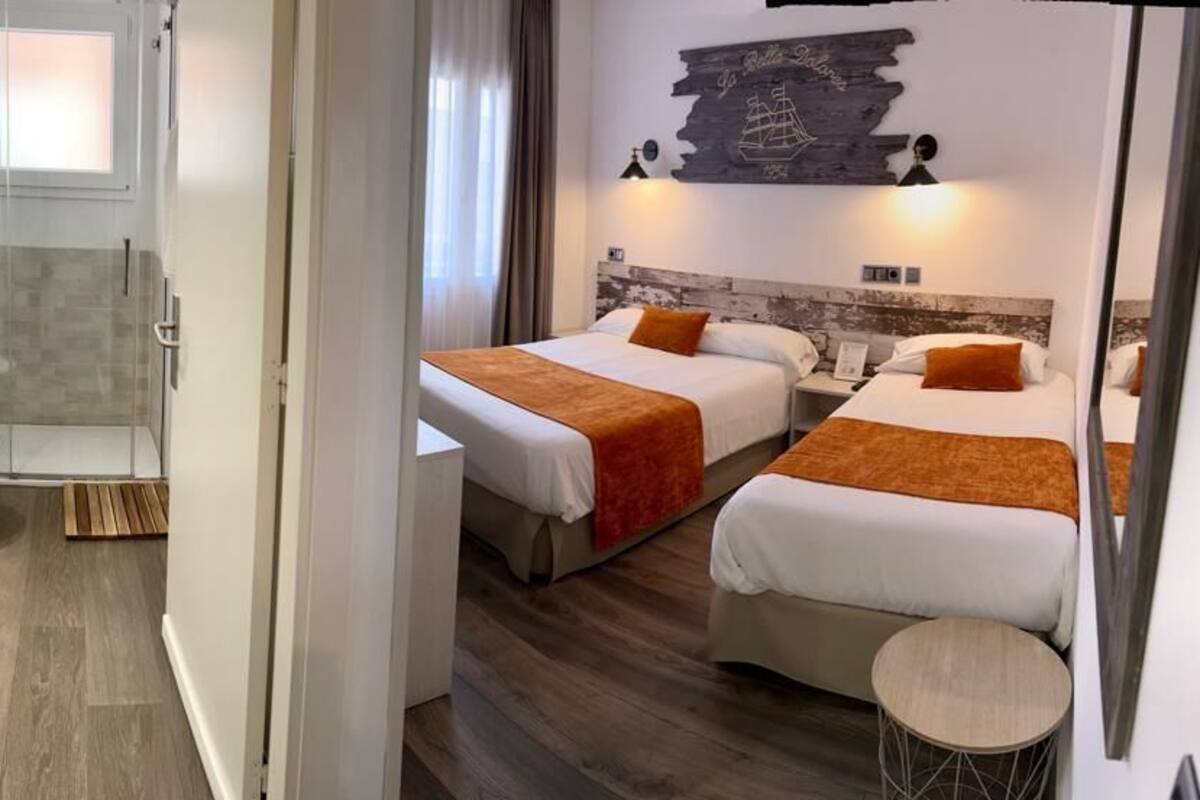 Habitación de hotel con dos camas, ducha, inodoro y una pequeña mesa redonda.
