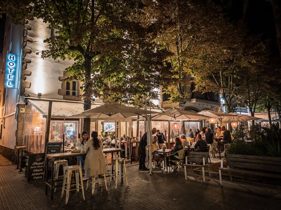 Un área de comedor al aire libre con mesas y sombrillas, un letrero de hotel y un edificio con fachada de piedra.