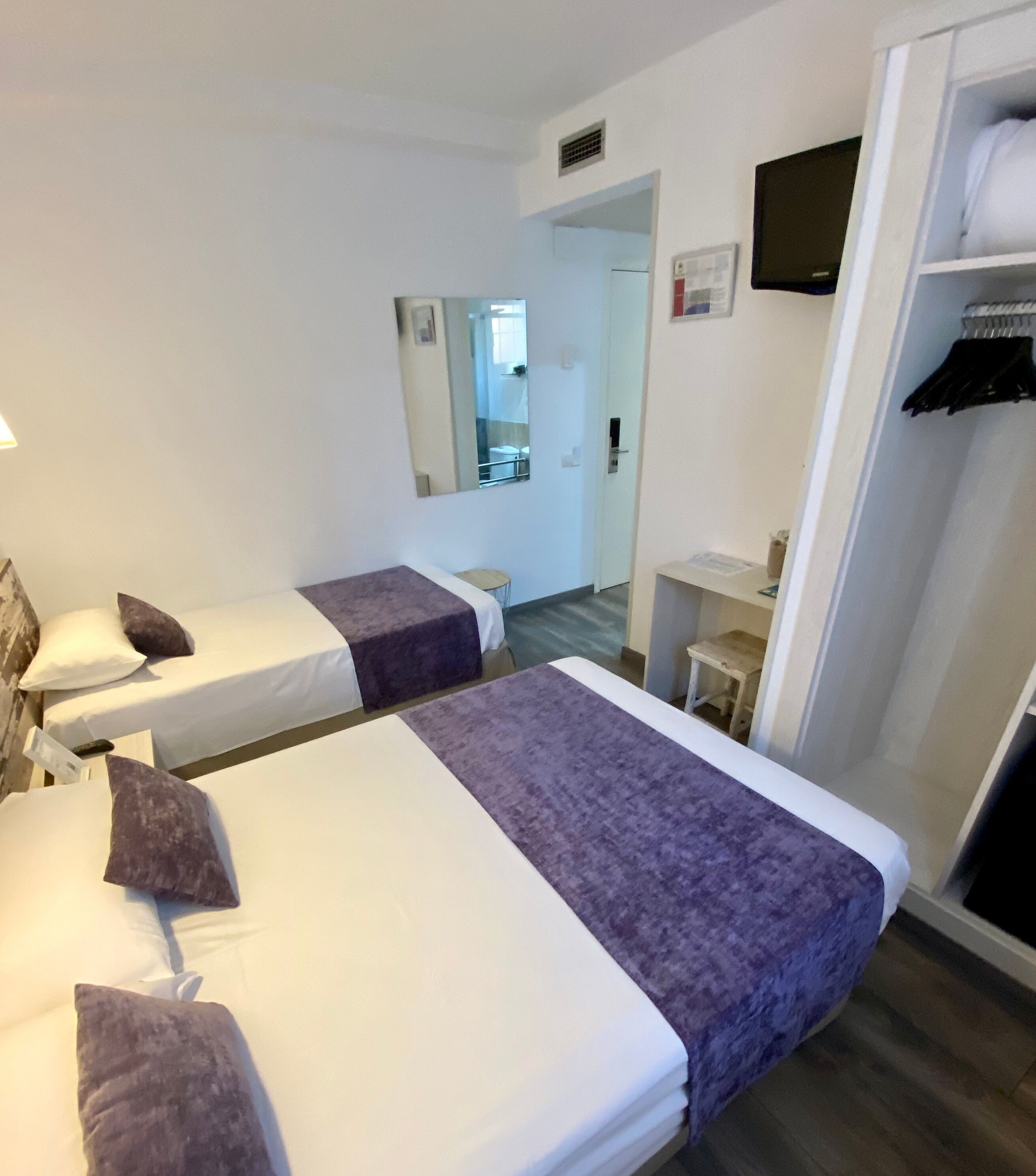 Una habitación de hotel con dos camas, un armario, un espejo y una televisión.