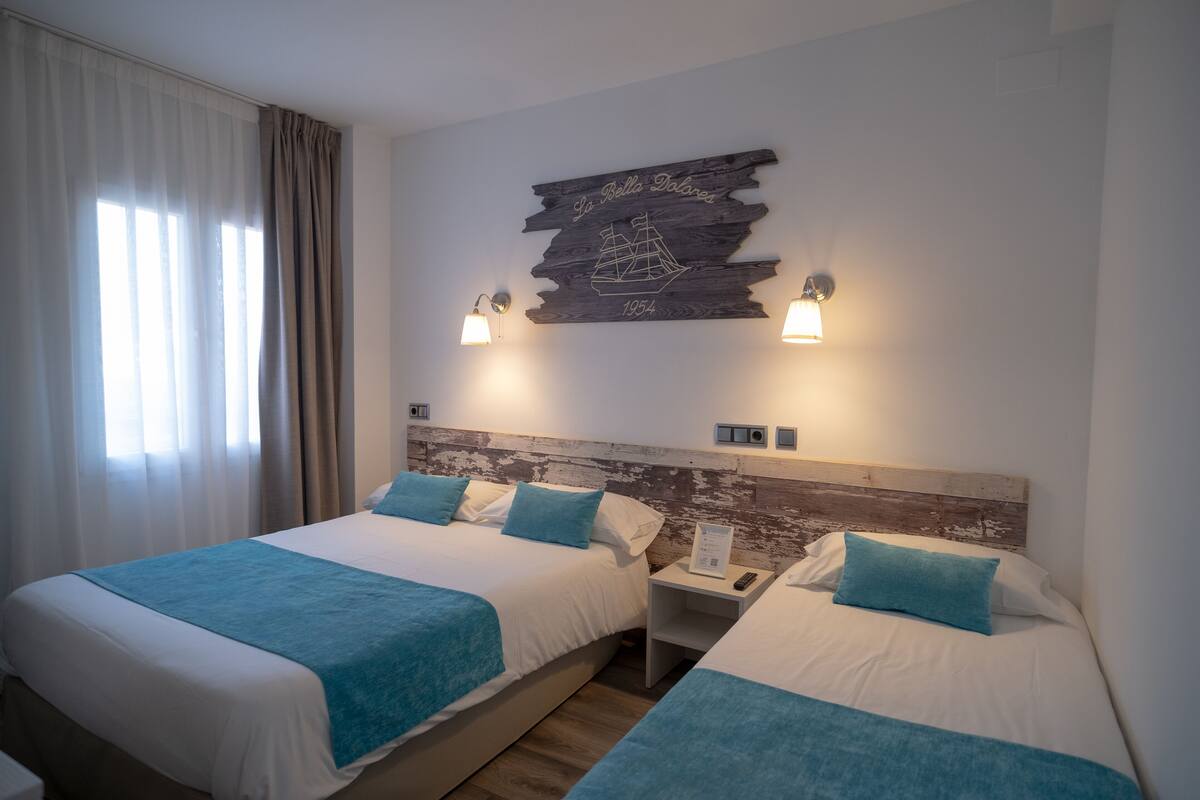 Habitación de hotel con dos camas, cada una con una manta azul, ropa de cama blanca y almohadas azules a juego. Hay un cabecero de madera con una ilustración de un barco y el texto 