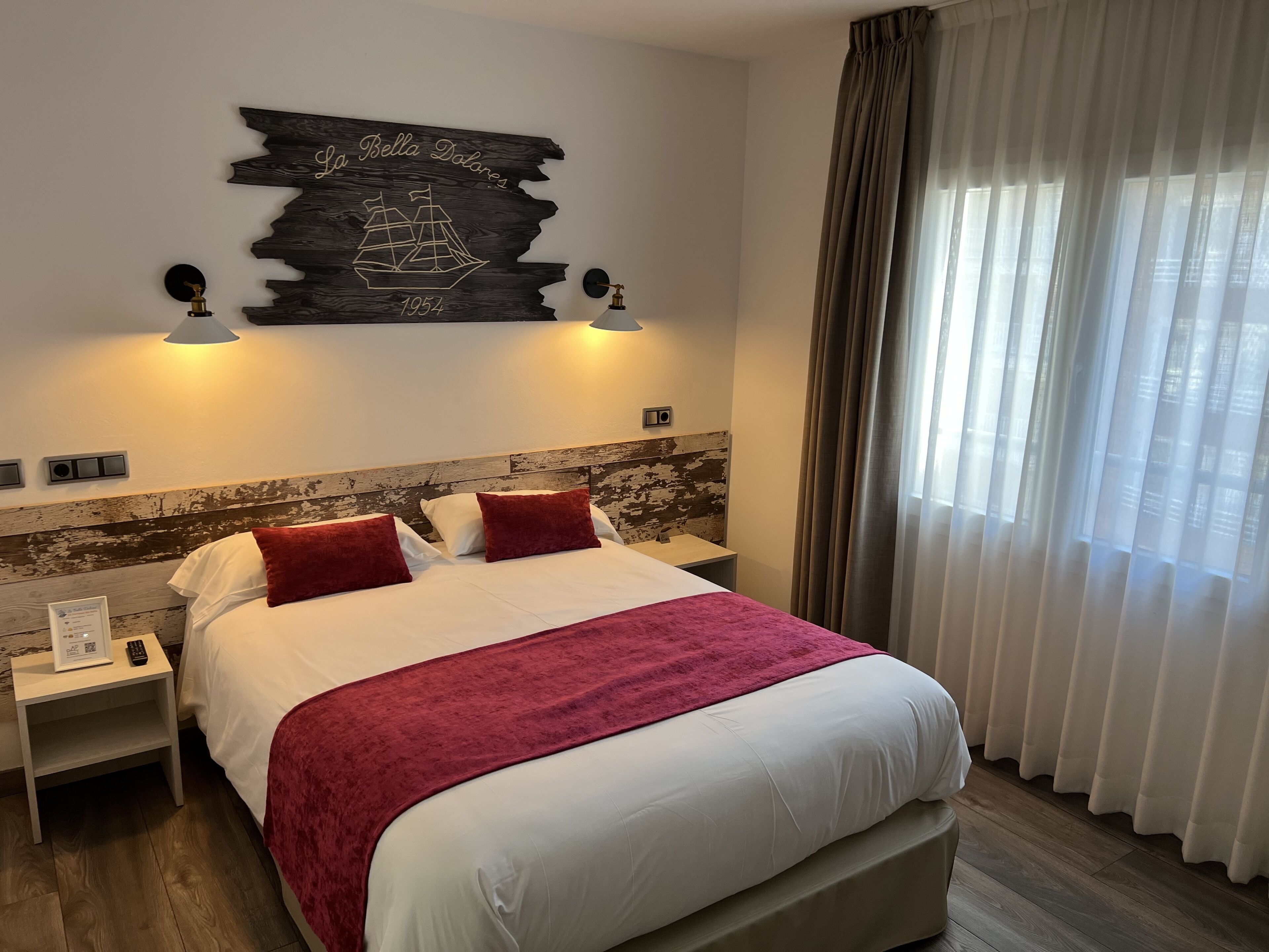 A hotel room with a large bed, two nightstands, a wall-mounted ship decoration, and a window with curtains.