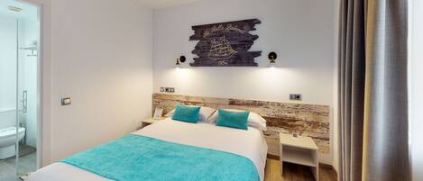 Habitación de hotel con cama, dos mesitas de noche, cabecero de madera, una obra de arte colgada en la pared y un baño visible a través de una puerta abierta.