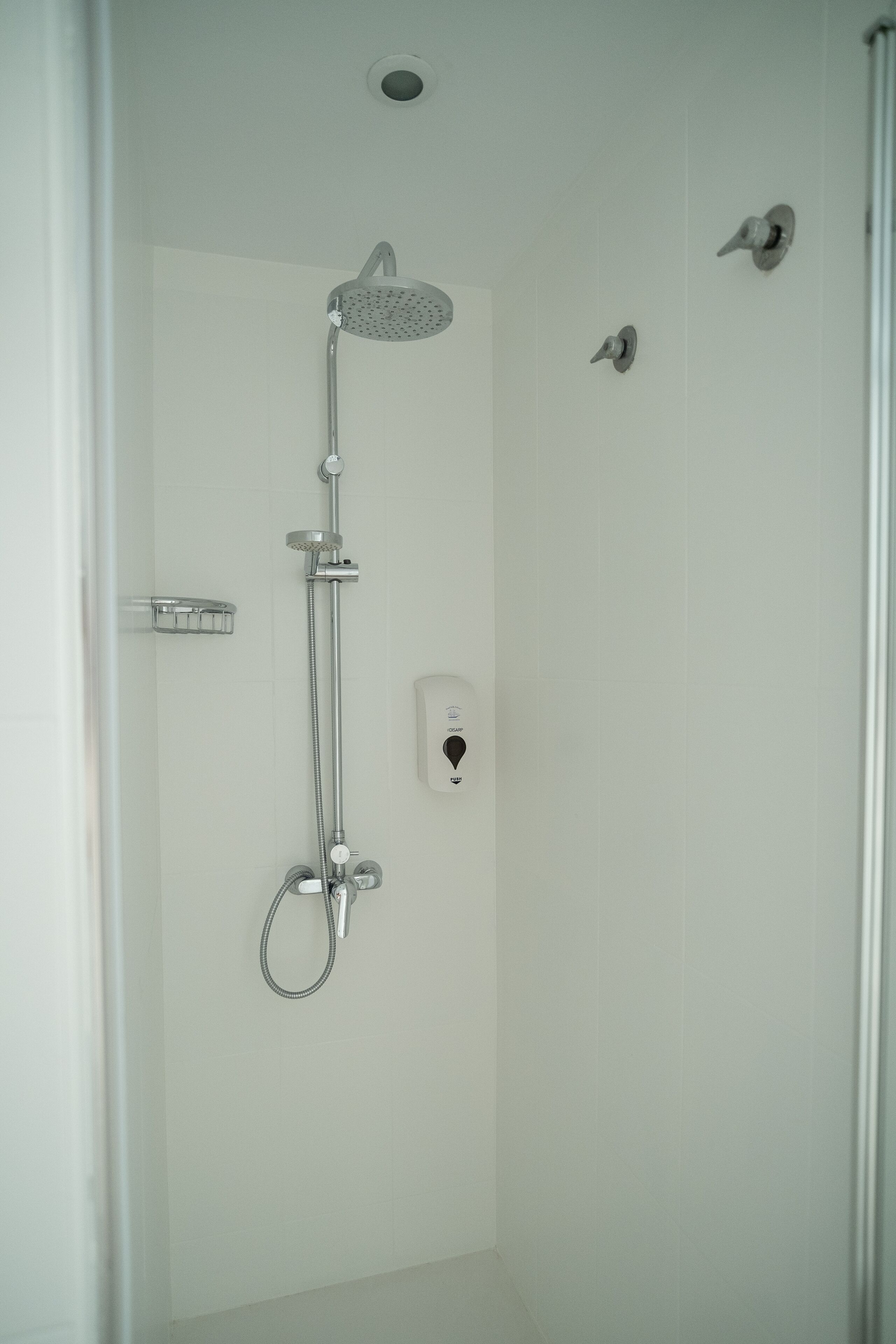 A shower with a handheld showerhead, a wall-mounted faucet, and a control panel.