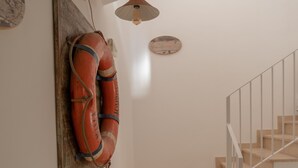 Eine Treppe mit beigen Stufen und weißen Geländern, ein an der Wand befestigter Rettungsring aus Holz und eine Deckenleuchte.