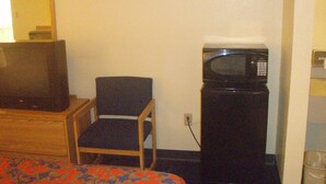 A small room with a bed, a television, a microwave, and a chair. - Pawnee Inn (Wichita)