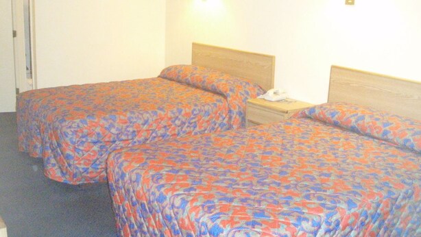 A hotel room with two beds, each with a patterned bedspread. There is a bedside table with a lamp and a phone. - Pawnee Inn (Wichita)