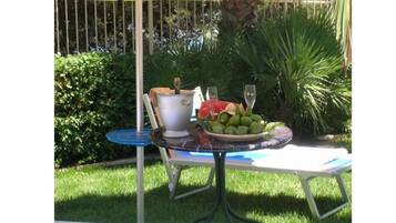An outdoor table with a white chair, a blue tablecloth, and a bowl of fruit.