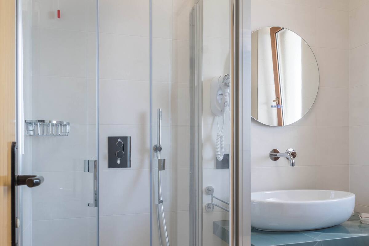 Une salle de bain moderne avec une douche à parois de verre, un lavabo blanc et un miroir rond.