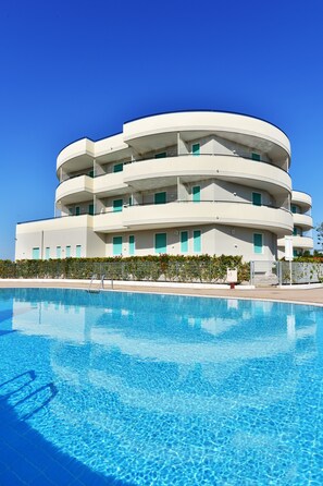 A modern multi-story building with a pool in front.