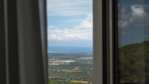 Uitzicht door een raam op een landschap met velden, gebouwen en een verre kustlijn.