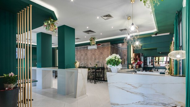 Een moderne hotellobby met een marmeren receptiebalie, groene wanden en een zithoek met een wand van baksteen.
