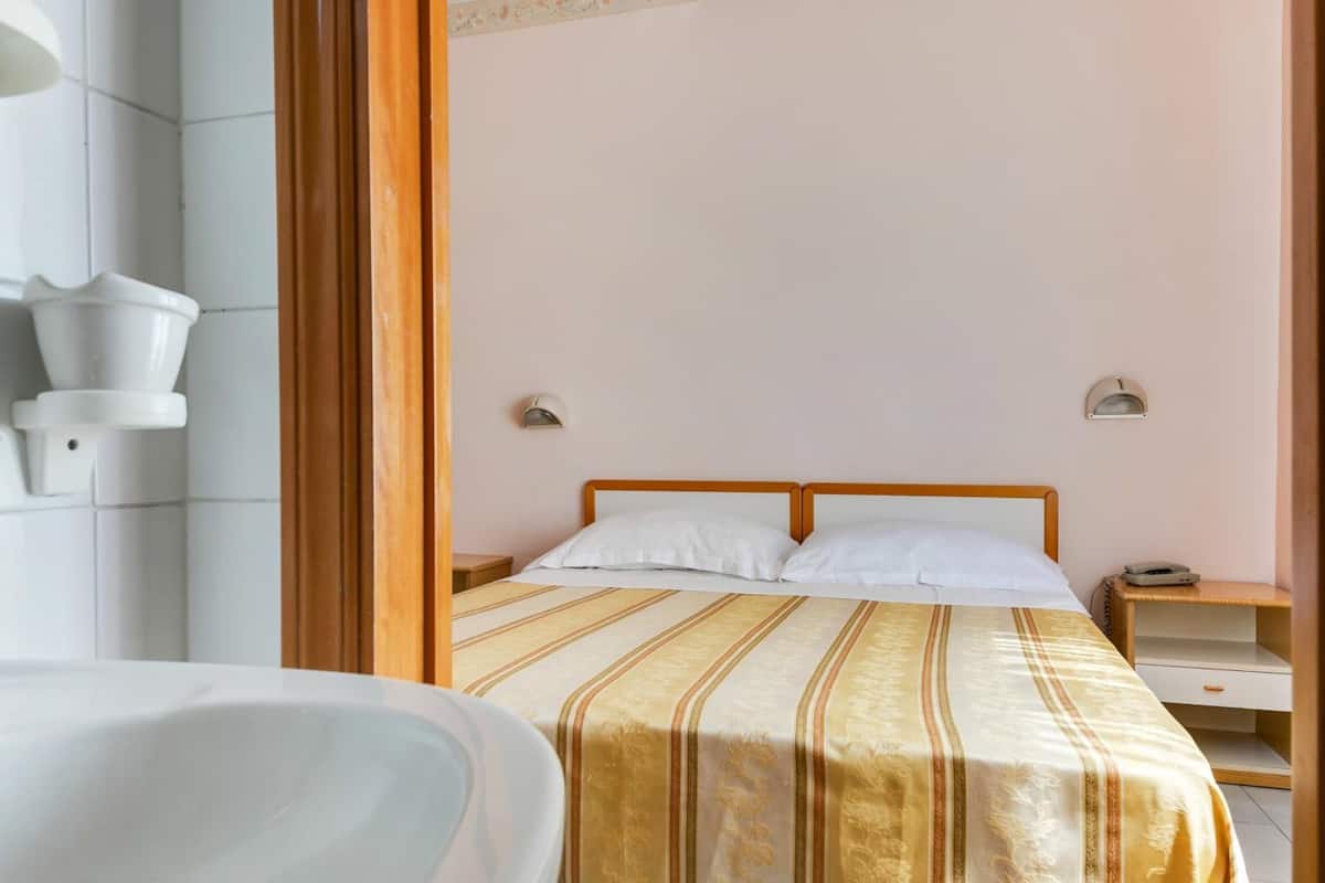 A hotel room with a bed, a nightstand, a bedside table, and a bathroom with a sink and mirror.