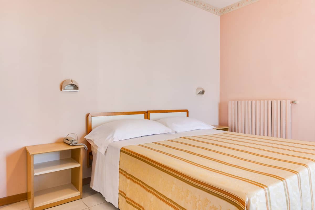A bedroom with a bed, a nightstand, a shelf, and a radiator.