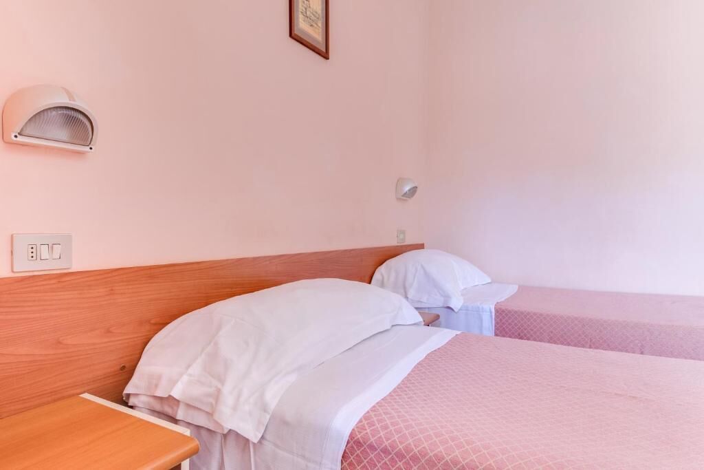 Een hotelkamer met twee bedden, een houten hoofdbord, een klein tafeltje en een wandradiator.