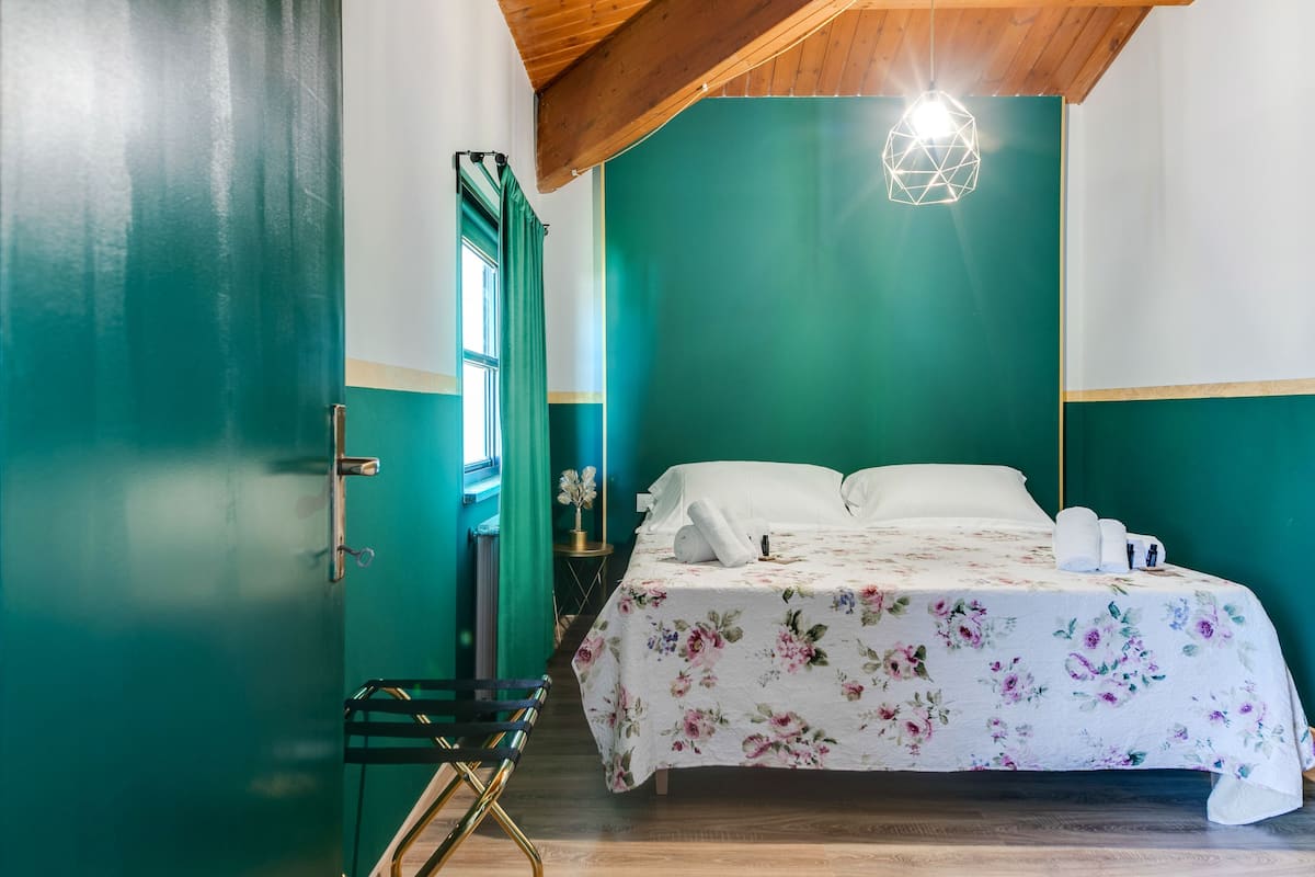 A bedroom with a bed, a chair, a nightstand, and a window.