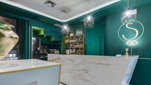 Een bar met een marmeren aanrecht, groene wanden en hangende geometrische lampen.