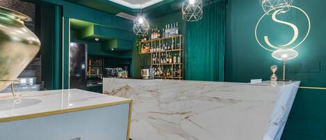 Zona de bar con encimera de mármol, paredes verdes y lámparas geométricas colgantes.