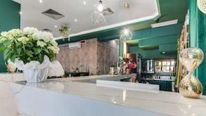 Een receptiezone met een marmeren balie, een groot boeket witte bloemen, en een bar met planken en een zandloper.