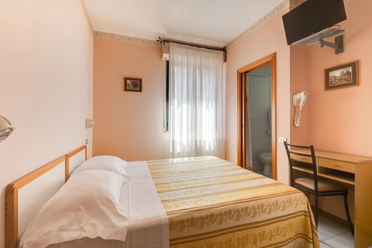 A bedroom with a bed, a desk, a chair, a TV, and a bathroom door.