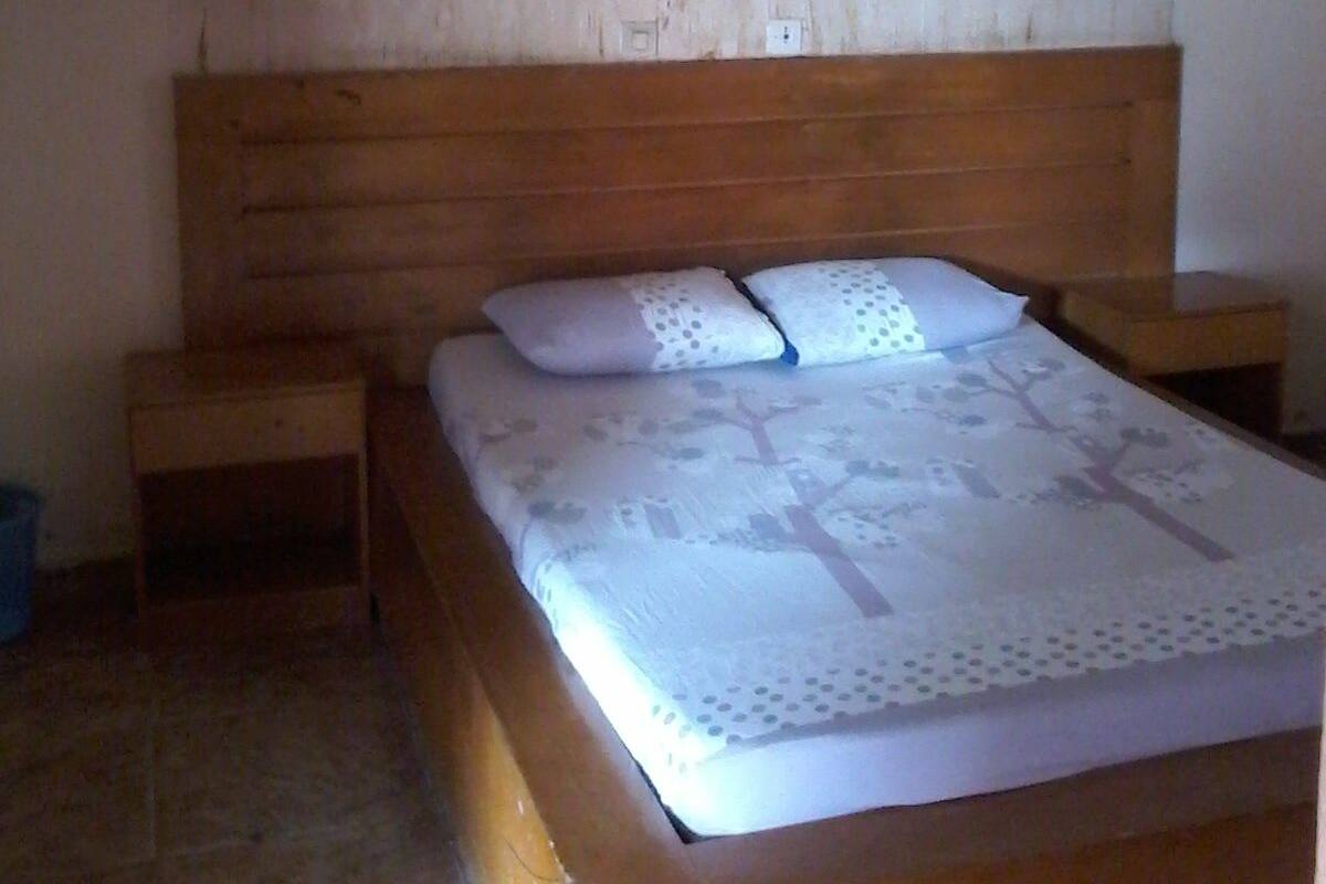 Un lit simple avec une tête de lit en bois, deux oreillers et une table de chevet de chaque côté.