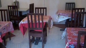 Un comedor con mesas cubiertas de manteles rojos, sillas de madera y un televisor de pantalla plana montado en la pared.