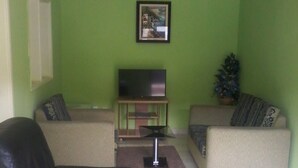 Una sala de estar con una pared verde, un sofá de cuero negro, un sofá color beige, un televisor sobre un mueble bajo y una pequeña mesa con una planta.