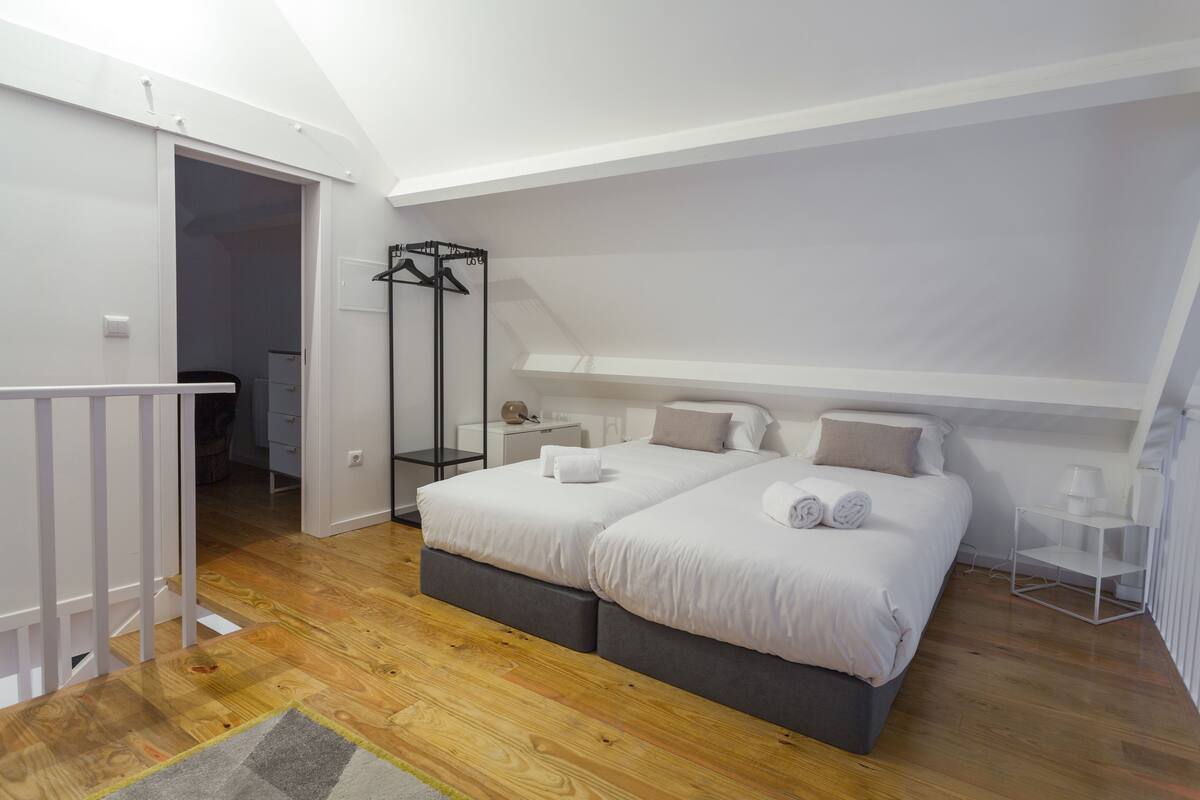 A bedroom with a loft-style ceiling, a double bed with white bedding, a bedside table, and a walk-in closet.
