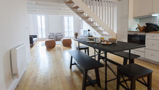A modern kitchen with a wooden staircase, a dining table with benches, and a view of the city through large windows. - City View - Santa Catarina (Porto)