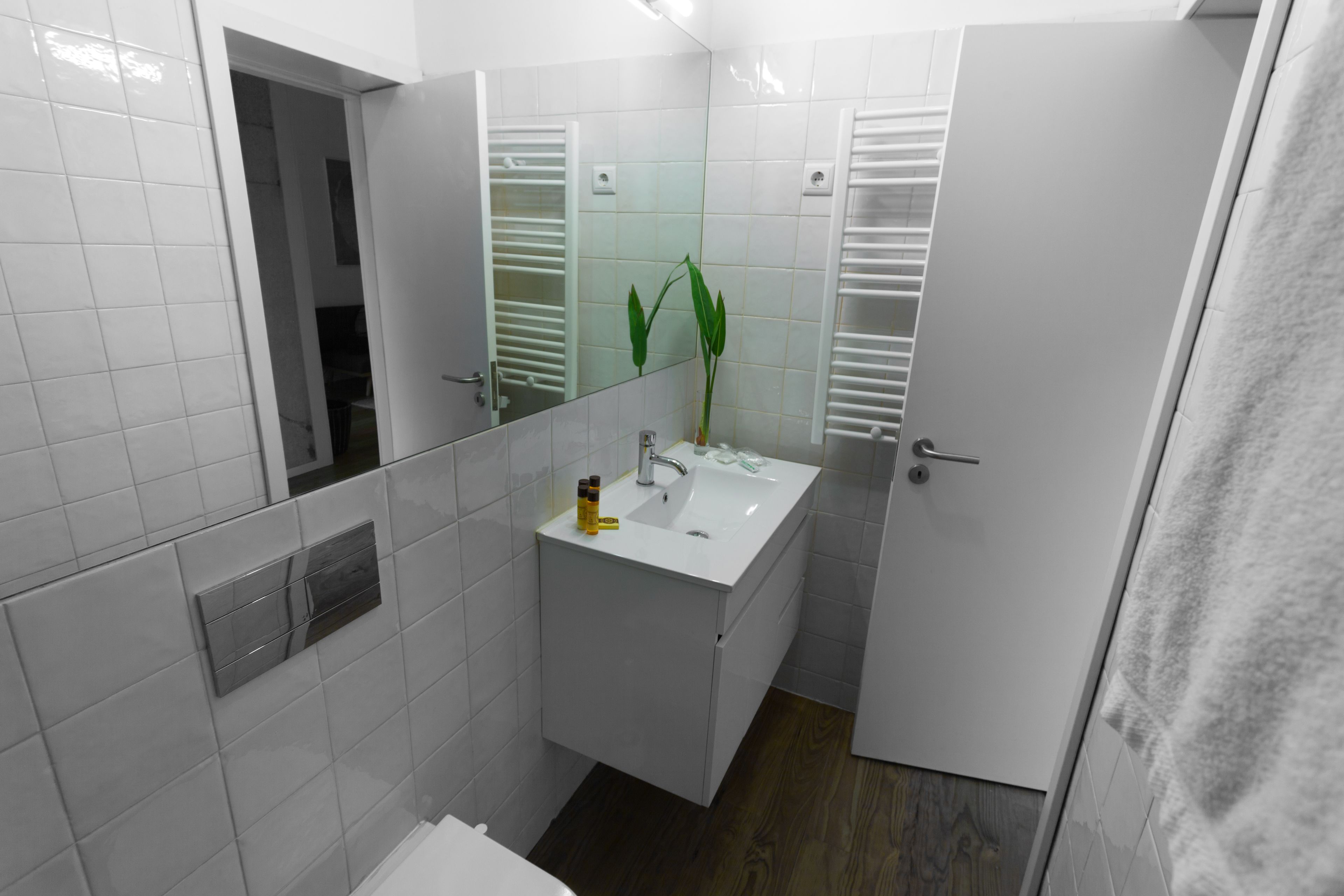 Une salle de bain avec des murs recouverts de carreaux blancs, un lavabo blanc, un miroir et un porte-serviettes.