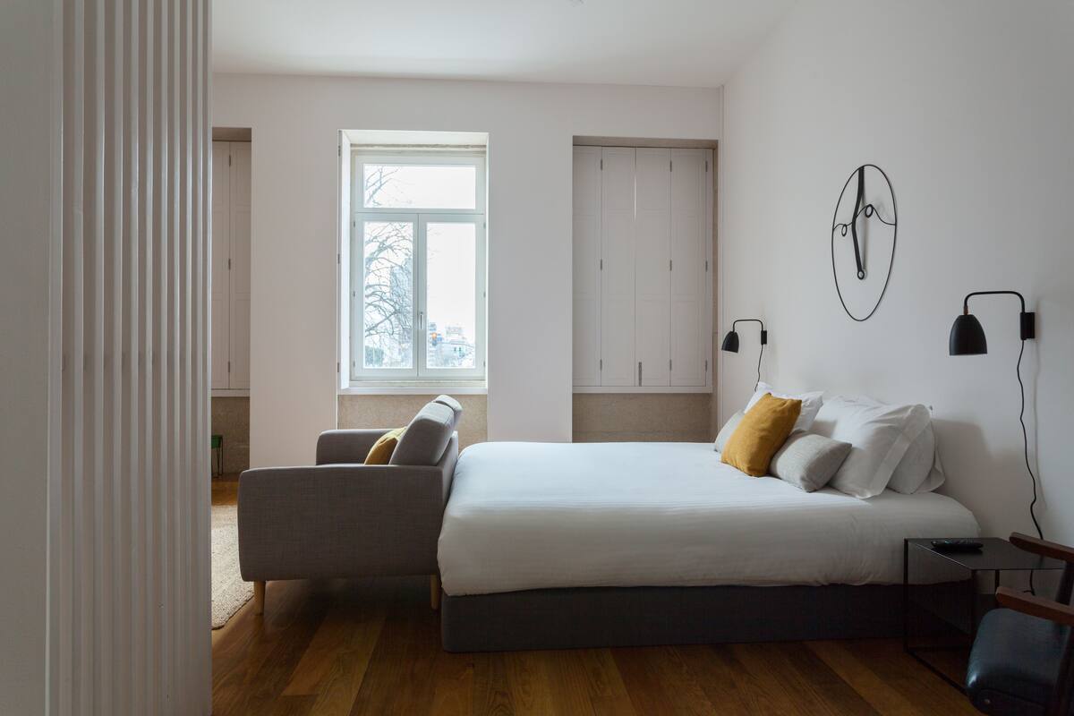 A bedroom with a bed, a chair, a nightstand, a window, and a wardrobe.