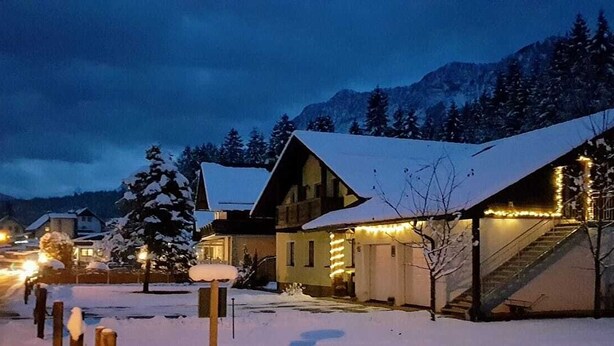 A snow-covered building with a staircase leading to a second floor, surrounded by snow and trees. - Apartments Winkler (Bad Goisern)