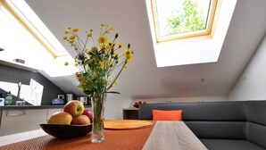 A modern kitchen with a skylight, a dining table with a fruit bowl, and a grey sofa with an orange pillow. - Apartments Winkler (Bad Goisern)