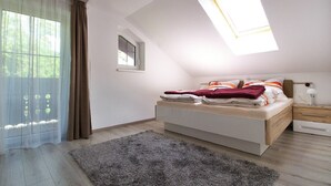 A bedroom with a sloped ceiling, a skylight, a bed with pillows, a bedside table, and a nightstand. - Apartments Winkler (Bad Goisern)