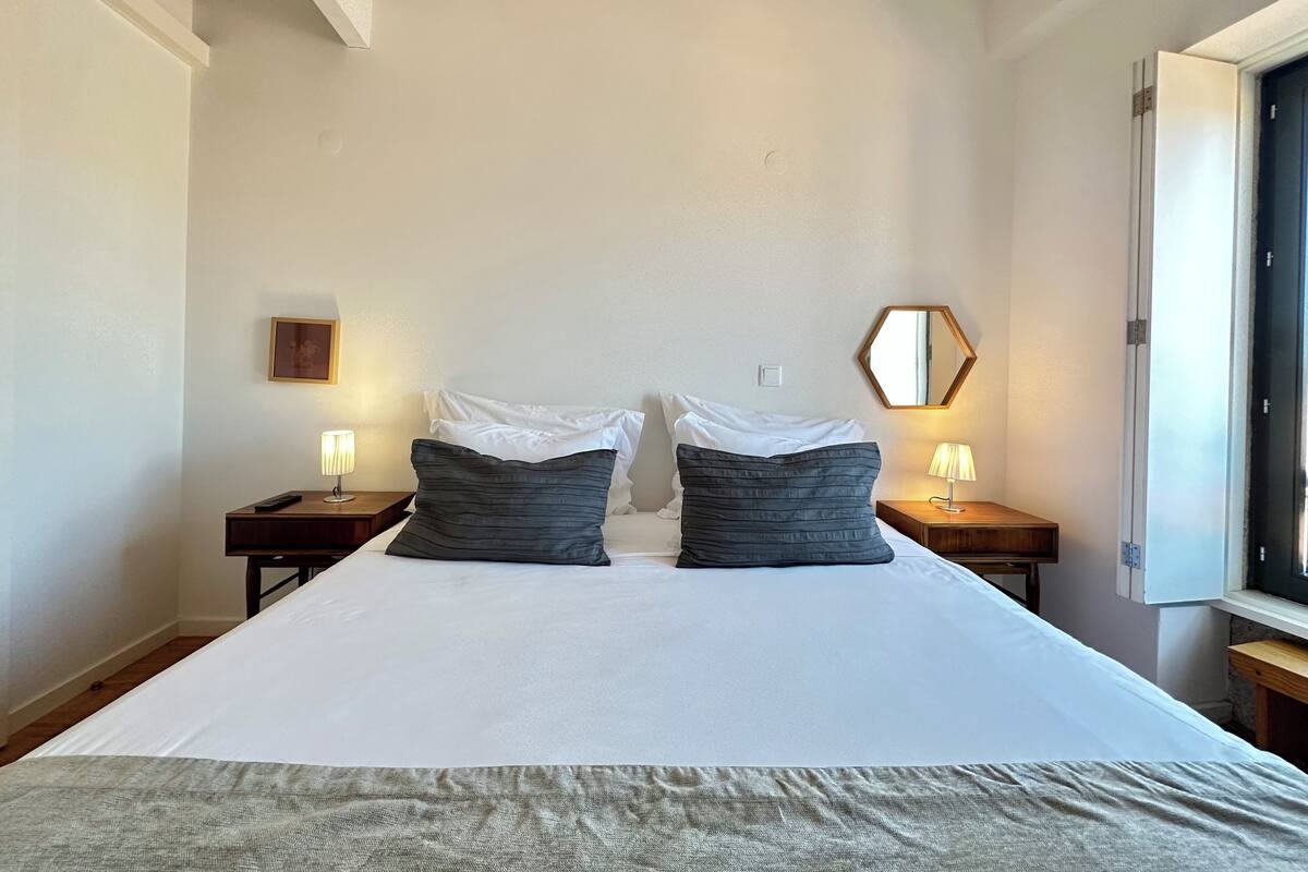 A hotel room with a large bed, two bedside tables, a nightstand, a mirror, and a window.