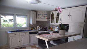 A modern kitchen with white cabinets, a marble-patterned floor, and a dining area with a table and chairs. - Chez Colombine (Chaponost)