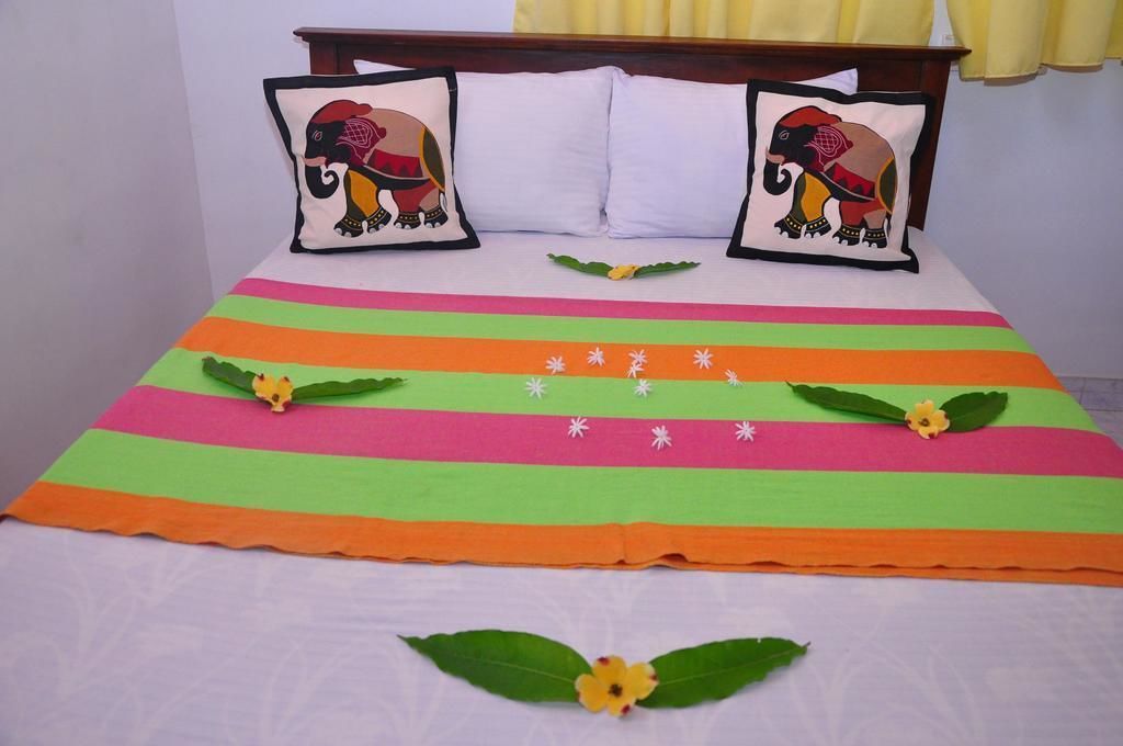 Una cama con ropa de cama a rayas coloridas, dos almohadas con diseños de elefantes y hojas y flores decorativas.