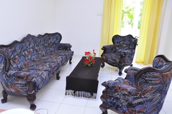 A room with a patterned sofa set, a matching armchair, and a small table with a vase of flowers.