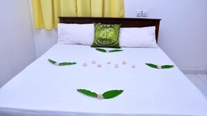 Una cama bien hecha con sábanas blancas, un cojín verde con un diseño de elefante y flores y hojas decorativas dispuestas sobre la cama.