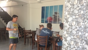 A dining area with wooden chairs and tables, a staircase, and a wall with a pebbled texture. - Lo hostel (Weligama)