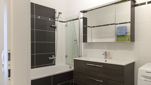 A modern bathroom with a glass-enclosed shower, a white sink with a mirror above, and a dark wooden vanity with drawers.