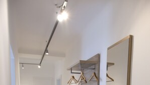 A hallway with a wooden bench, a black mat, a wooden dresser, and a mirror with wooden hangers.
