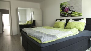 A modern bedroom with a large bed, a wardrobe, and a mirror.
